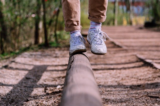gros plan sur les chaussures d'une personne qui marche en équilibre sur une poutre en bois